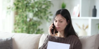 Osoba na kanapie trzymająca dokument i telefon podczas zgłaszania reklamacji błędnego naliczenia bankowego