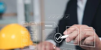 Dłoń zaznaczająca elementy cyfrowej dokumentacji obok kasku i laptopa jako kontekst błędów przy pozwoleniu na budowę